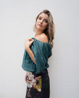 Woman wearing a teal off-shoulder bubble hem top with a floral skirt against a white wall.