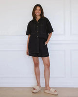 Woman wearing black 100% cotton high-rise shorts with contrast stitching, elastic waistband, and drawstring tie.