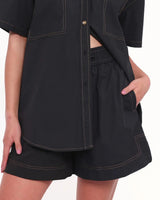 Black high-rise cotton shorts with an elasticised waistband, drawstring tie, and contrast stitching detail.
