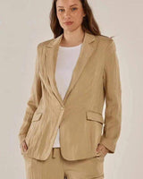 A woman wearing a relaxed-fit, tan drapey Sutton blazer with functional pockets and a single-button closure.