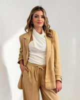 Woman wearing a relaxed-fit, tan drapey Sutton blazer with functional pockets over a white sleeveless top.