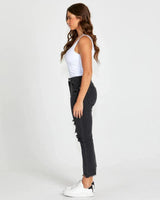 Model wearing black mid-rise distressed Suzi jeans with a slim fit, raw hem, and ripped details.