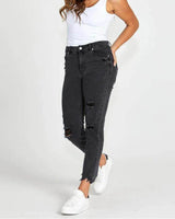 Mid-rise black distressed jeans with rips and a raw hem, styled with a white tank top and sneakers.
