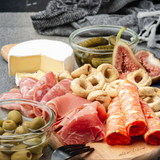 Assorted cured meats, green olives, soft white cheese, sliced figs, cornichons, and Tarallini - Olive Oil round crackers on wooden board