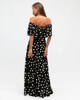 Woman wearing a black off-shoulder rayon maxi dress with a white polka dot print and flowing tiered skirt.