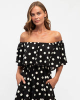 Model wearing a black off-shoulder maxi dress with white polka dots, crafted from soft rayon with a flowing silhouette.