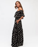 Model wearing a black and white polka dot off-shoulder rayon maxi dress with a tiered flowing skirt.