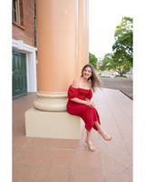Woman wearing a red stretch crepe Victoria event dress with puff sleeves and a ruched front, sitting by a large pillar.