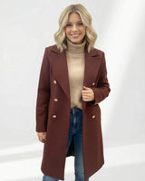 Brown wool-blend Vivian coat featuring double-breasted gold buttons, worn over a beige turtleneck and blue jeans.