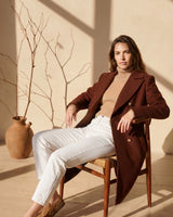 Elegant brown wool-blend Vivian coat featuring gold buttons, worn over a beige turtleneck and white jeans.