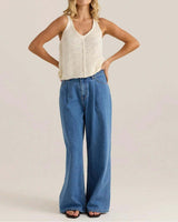 Model wearing blue wide-leg denim jeans with front pleats and functional pockets, paired with a cream knit tank top.