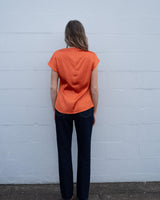 Back view of a burnt orange satin top with short cap sleeves and an invisible back zipper, worn with dark jeans.