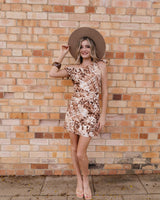 Woman wearing a brown animal print cotton cold-shoulder mini dress with a wide-brim hat against a brick wall.
