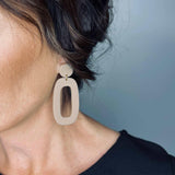 Close-up of Riley Dangle Earrings made of lightweight, durable beige acrylic with an organic shape on a woman's ear